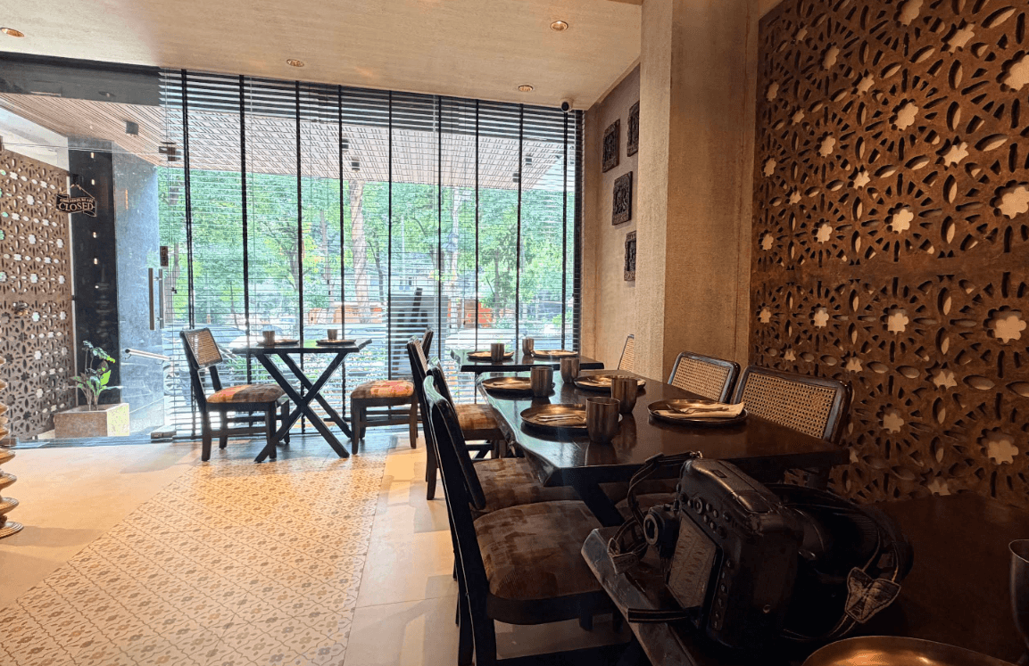 Inside Kopparrai: carved jaali wall, cane chairs and wooden tables